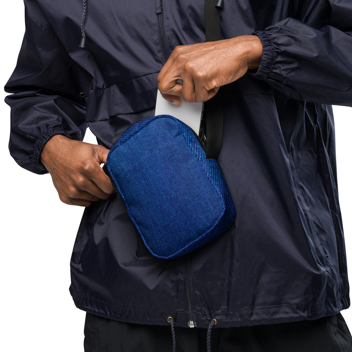 Denim crossbody bag worn at the hip, phone being slipped into the front pocket
