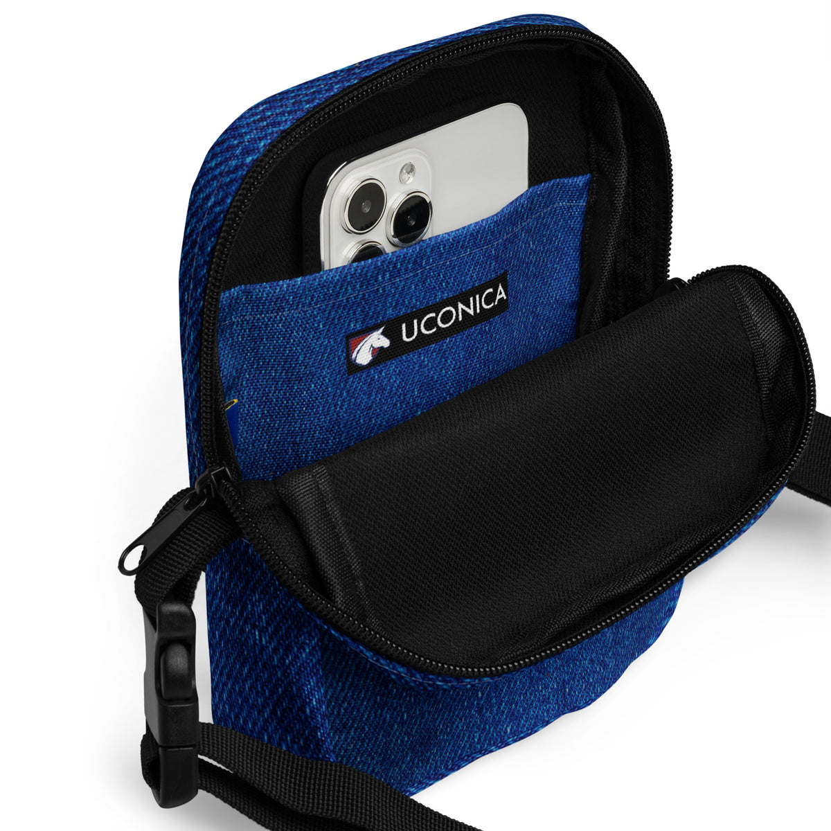 Denim crossbody bag open, phone inside the padded interior beside the Uconica label